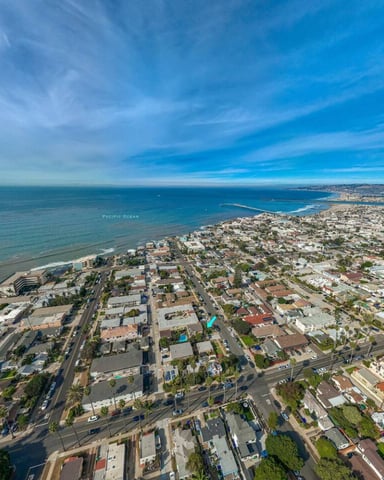 Aerial view of coastal residential neighborhood with Pacific Ocean, sandy beach, and distant bay under blue sky