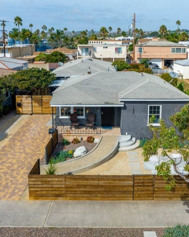 Modern gray single-story home with patio, wooden fence, and palm trees in residential neighborhood