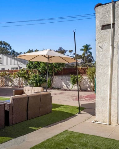 Backyard patio with rattan seating, umbrella, lawn, and laundry room door on right