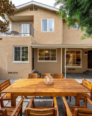 Backyard patio with wooden dining table, stone fountain, and two-story tan house with upper balcony