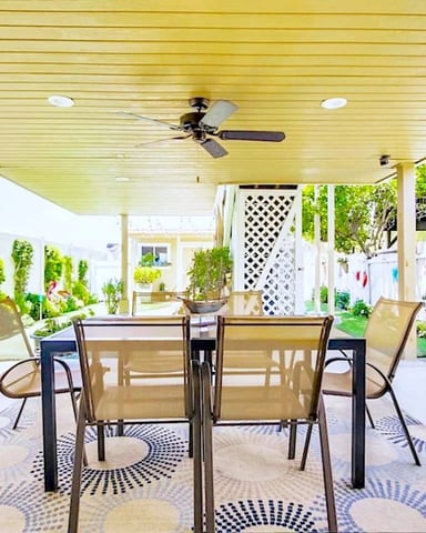 Covered patio with yellow ceiling, dining table, chairs, built-in grill, and surrounding garden planters